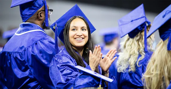 Madison College graduate smiling and clapping wearing blue cap and gown