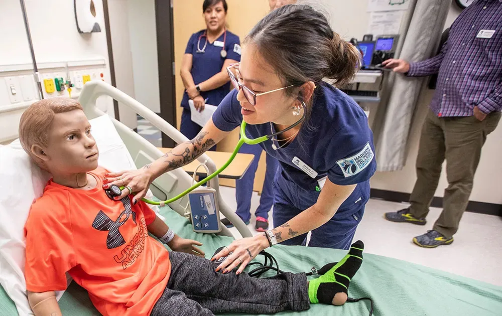 Nursing student practicing with stethoscope on child manikin