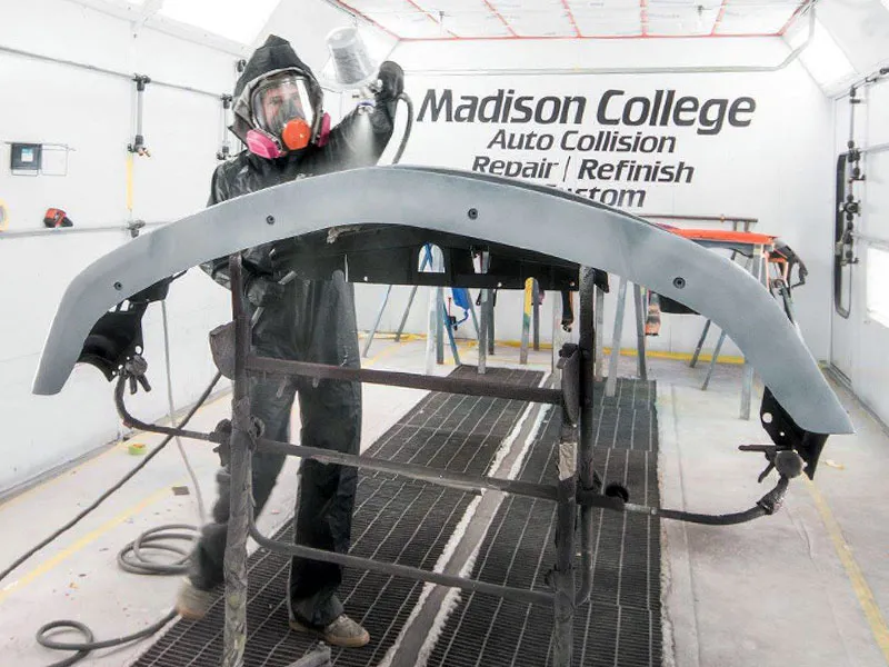 student applying primer to a car bumper in an auto paint booth