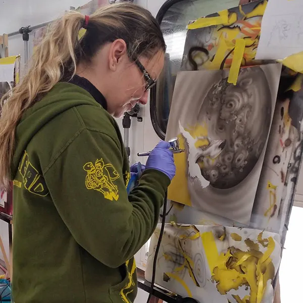 student practicing airbrush techniques on a metal panel