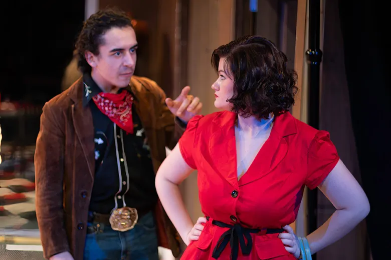 A man in western attire points at a woman in a red dress in a scene from Bus Stop