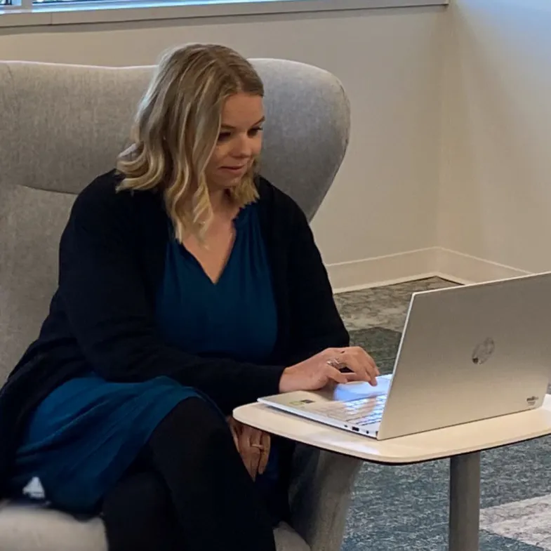 Carrie, Accounting program alumni, sitting in a chair typing at a computer