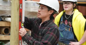 Student in a hard hat with a level on a piece of wood.