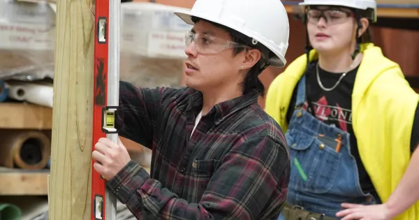 Student in a hard hat with a level on a piece of wood.