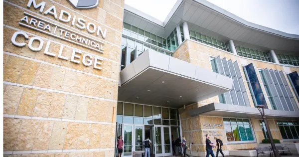 Gateway entrance of Truax building with logo name in front and students walking into the building with backpacks on.