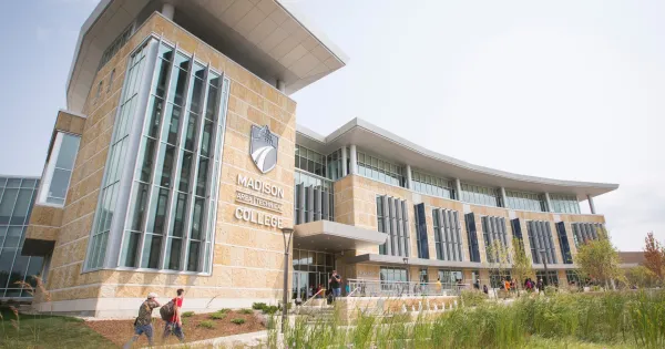 Exterior shot of Gateway entrance with two students walking on path, with purple flowers blooming nearby.