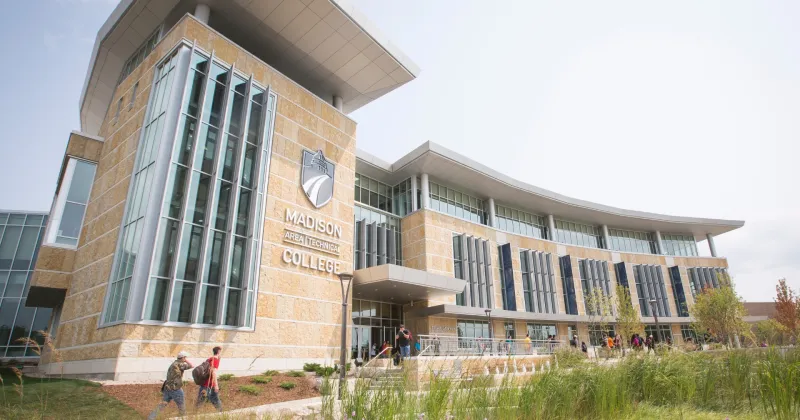 Exterior shot of Gateway entrance with two students walking on path, with purple flowers blooming nearby.