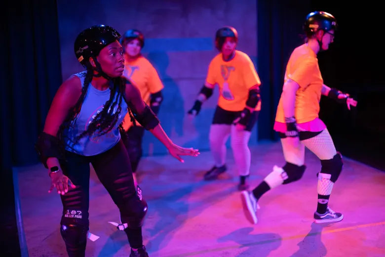 Four actors wearing helmets and knee pads in a scene from the Roller Derby Play