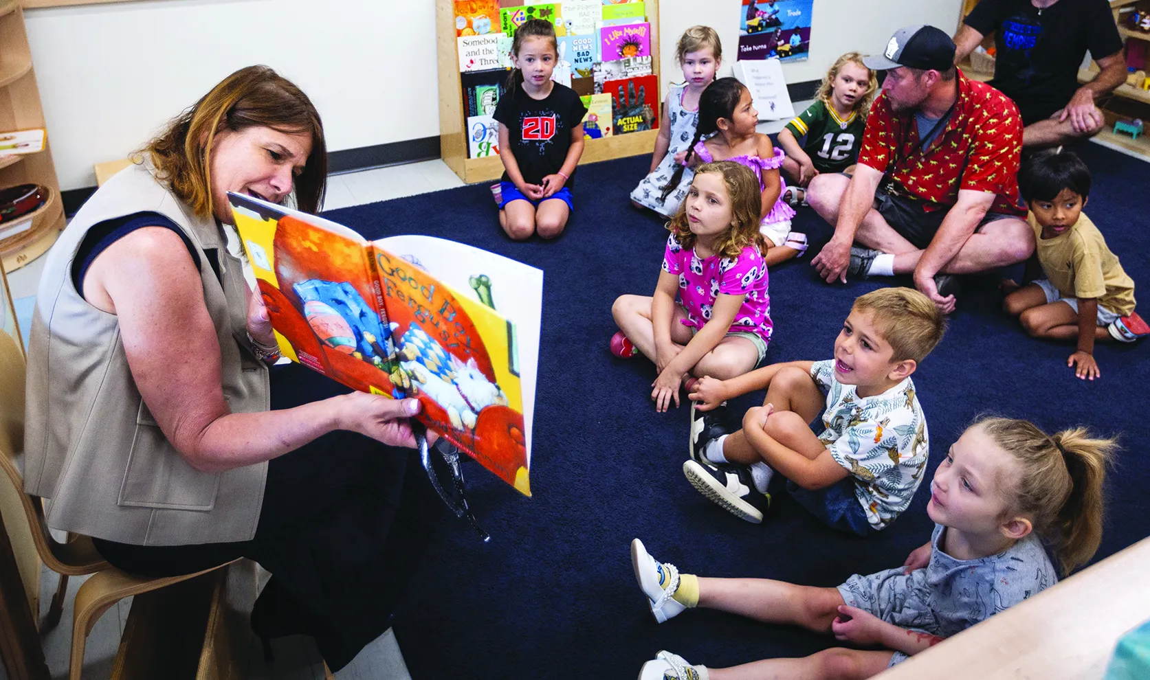 President Berne holding a storybook and reading from it while children sit on the floor, listening to her.