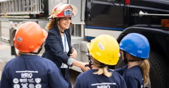 President Berne, wearing a firefighter helmet, shakes hands with young girls in the CampHero program.