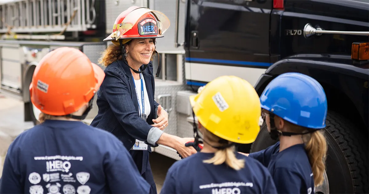 Dr. Berne shaking hands with students and smiling while wearing a firefighter's hat