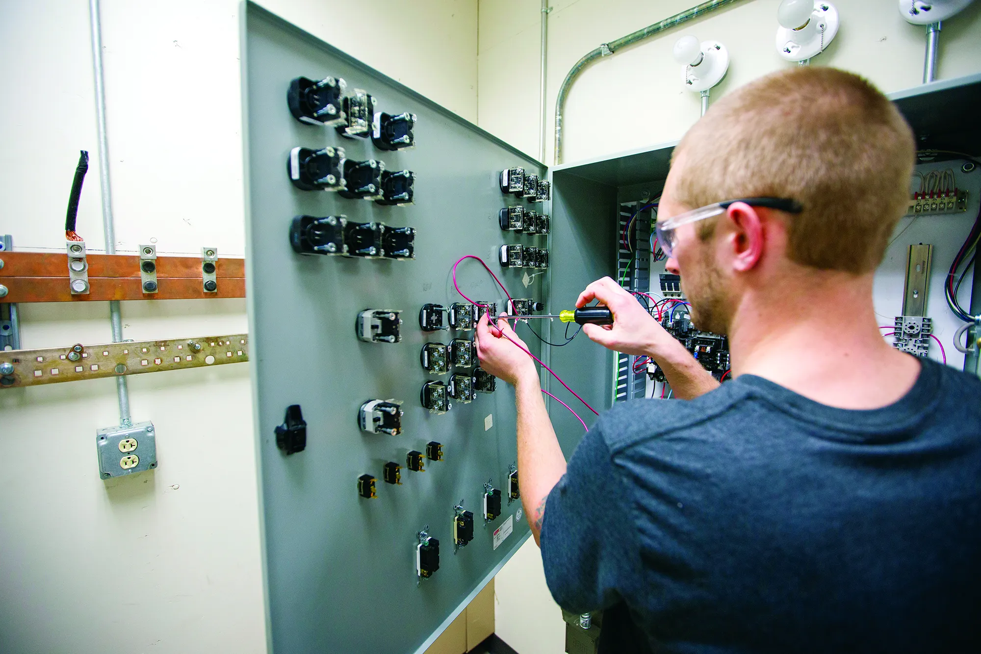 Male apprentice student making adjustments with a screwdriver in a grey electrical box.