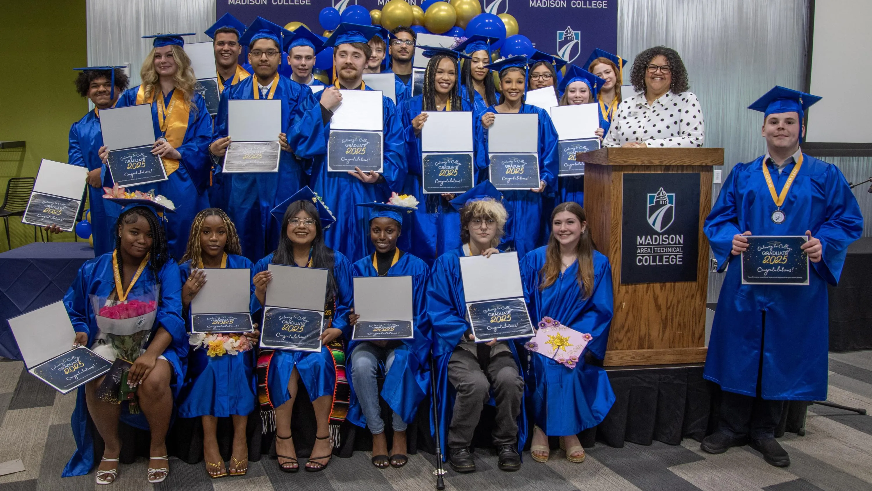 A group of Gateway to College graduates, dressed in blue caps and gown, holding their diplomas and certificates.