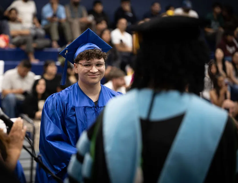 Graduate in blue cap and gown, smiling.