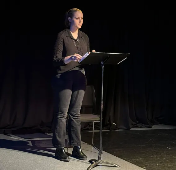 A young woman on an stage reading from a music stand