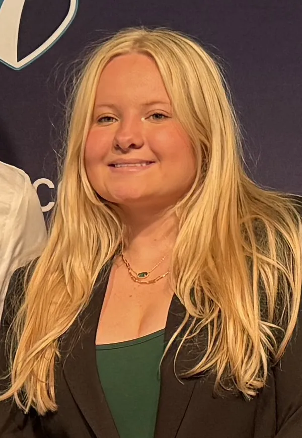 Haldey Strang, blond hair, smiling, wearing dark blazer and green shirt.