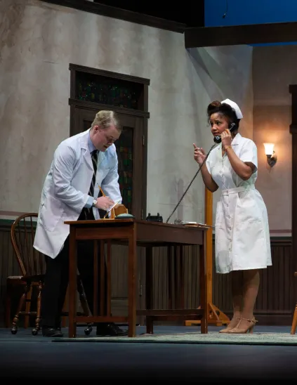 A nurse talks on a black corded phone while the doctor takes notes in a scene from the play Harvey