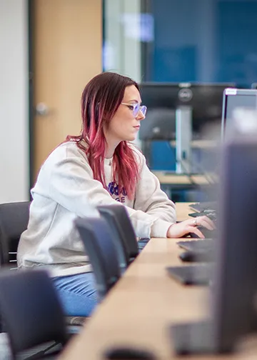 madison college student sitting at a computer in a lab. Looking at screen with hand on mouse. 