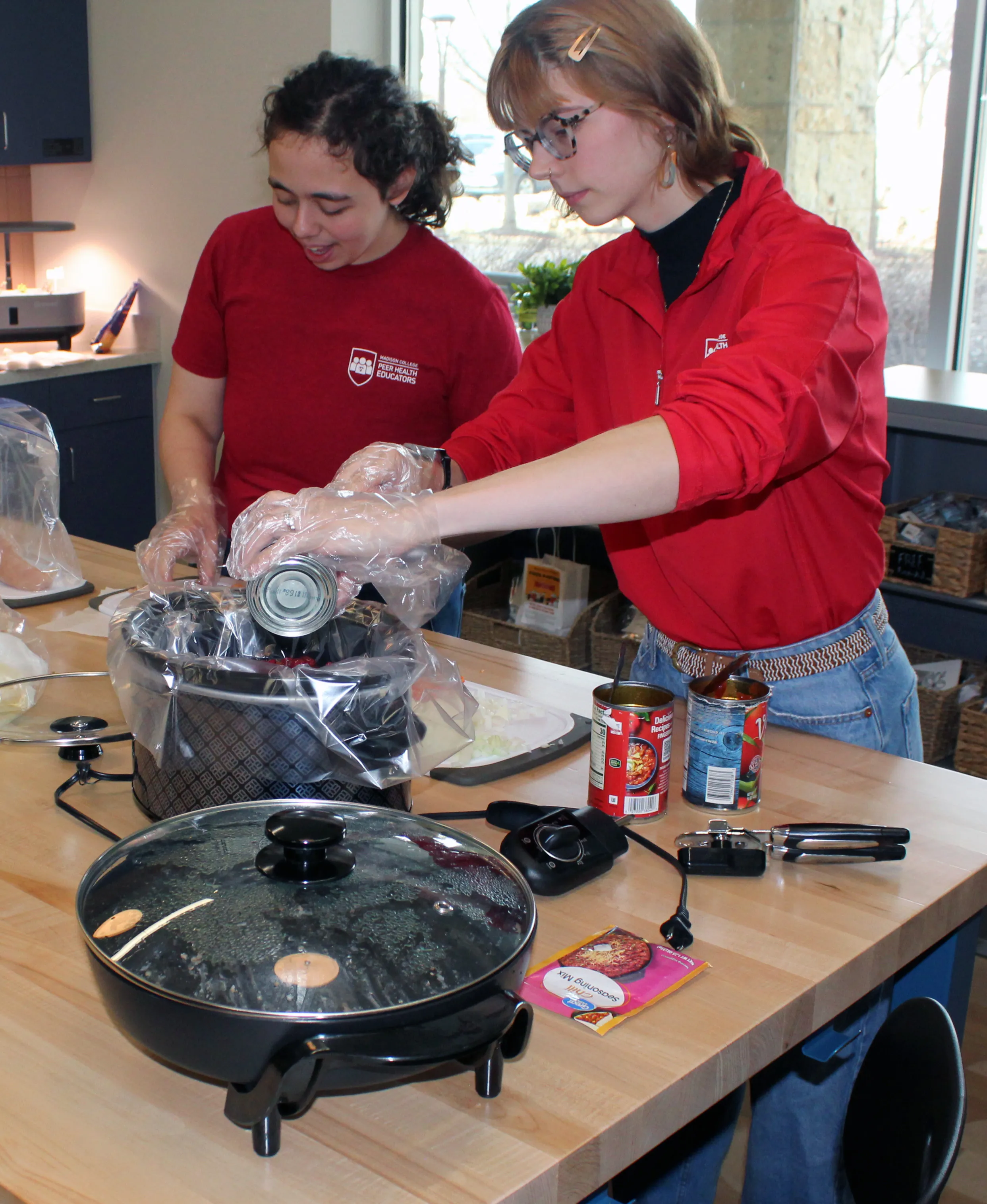 Two students emptying cans into a crock pot and chopping vegetables.