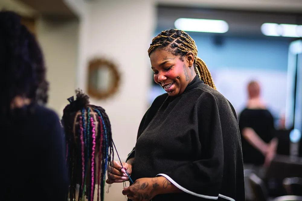 Myra Crump in classroom working on a model head, combing out braids.