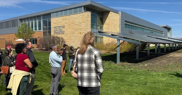People standing outside a building on Truax campus, looking at solar panels. Blue skies are in background, green grass in foreground.