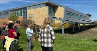 People standing outside a building on Truax campus, looking at solar panels. Blue skies are in background, green grass in foreground.