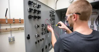 Male apprentice student working with a screwdriver on a gray electrical box.