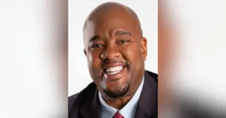 Black man with beard and mustache, wearing a dark blazer, and smiling.
