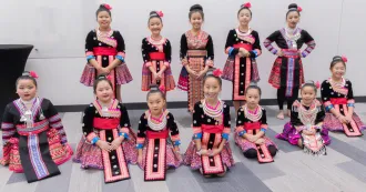 A group of young girls posing in rows, wearing colorful Hmong costumes with black, blue, pink and red colors.