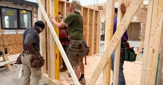 Construction and remodeling students working in a house frame, hammering wood.