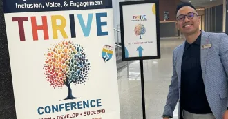 Madison College administrator smiling, wearing blue blazer, standing next to Thrive Conference placard.