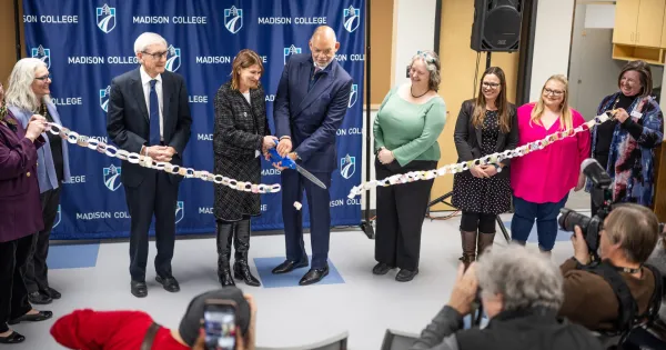 Madison College President Dr. Jennifer Berne, former President Dr. Jack Daniels, Gov. Tony Evers and other officials cut a ribbon and smile for a photo.