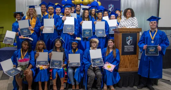 Group of Madison College Gateway to College graduates, wearing blue caps and gowns, holding diplomas, posing for a photo.
