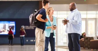 A male advisor talking with a parent and student in the hallway of Truax campus, with door and window in the background.