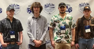 Four male students posing in front of a PAS national conference banner.