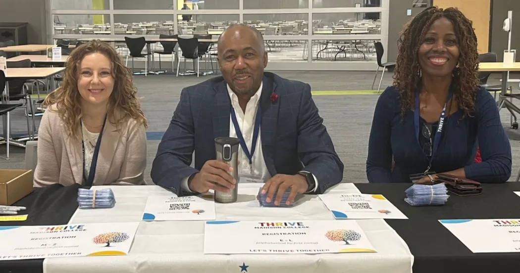 Three people sitting at conference check-in table, smiling, and wearing conference badges.