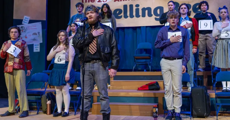 Group of 10 actors on stage of spelling bee musical, performing with hands at their heart, saying the Pledge of Allegiance.