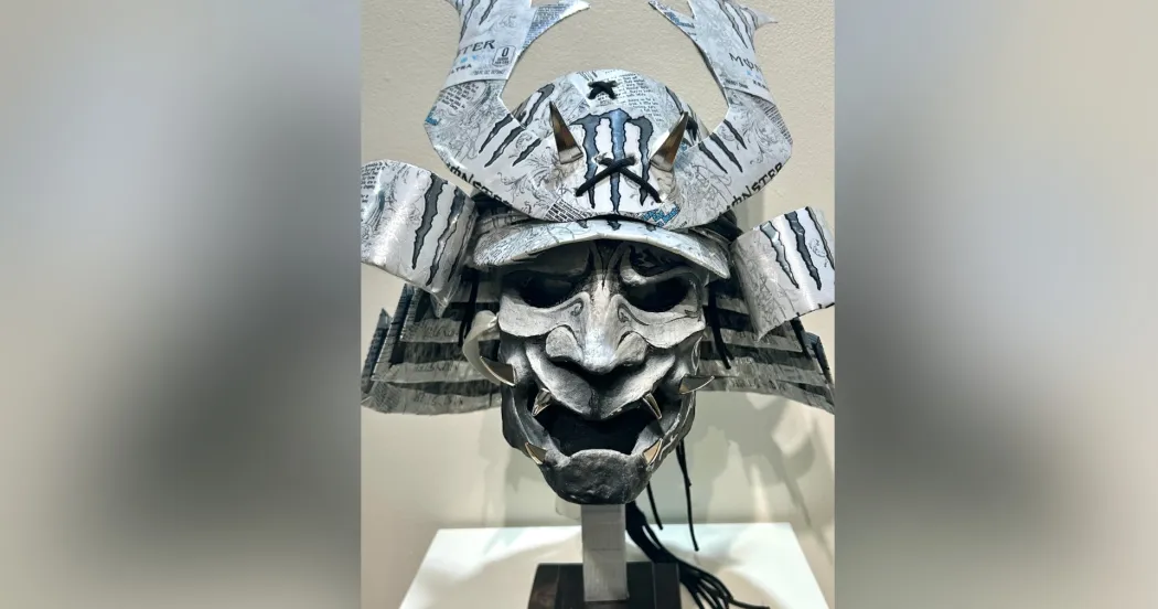 Gray metal sculpture with wide eyes and mouth, and horn like structures coming out of head.
