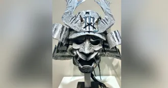 Gray metal sculpture with wide eyes and mouth, and horn like structures coming out of head.