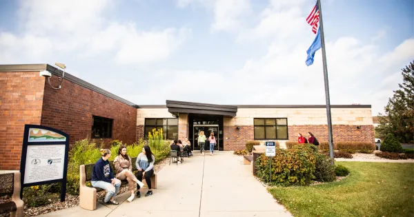 Exterior entrance of Reedsburg campus with light red brick and students sitting on bench outside.