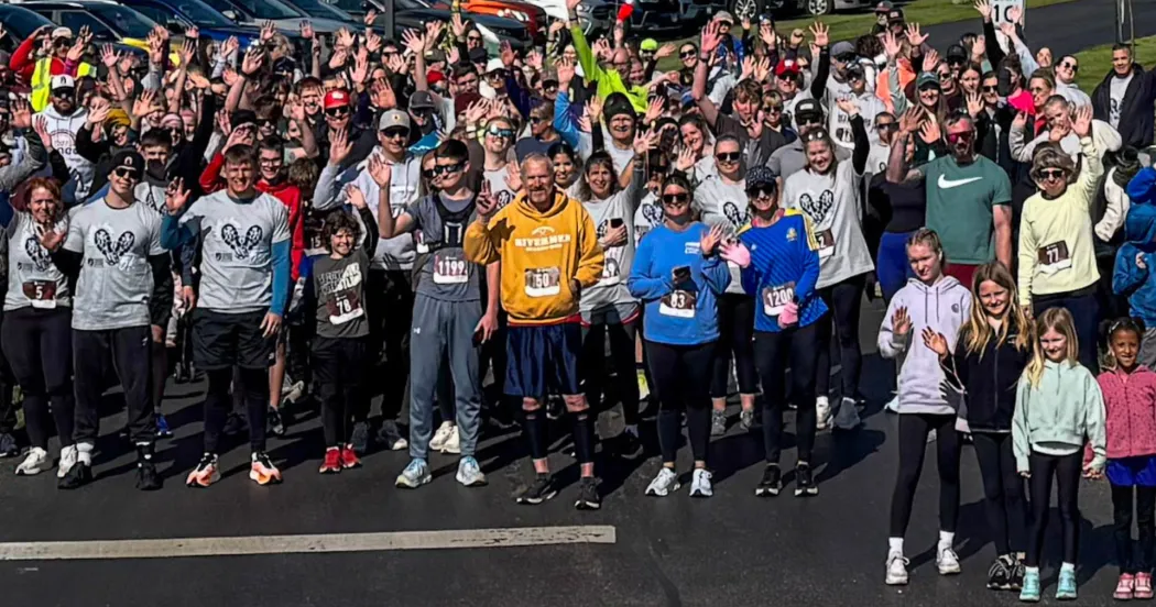 Runners and walkers, wearing colorful T-shirts and sweatshirts, lined up near a starting line.