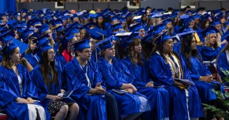 Graduates with blue cap and gown, sitting in rows, in a ceremony.