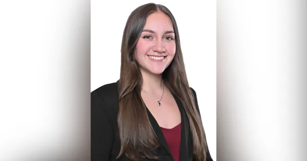 Woman with long brown hair, black blazer and red shirt, smiling.