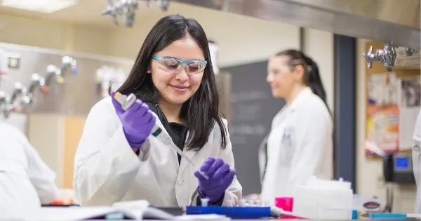 Woman with black hair and white lab coat, working with a syringe.