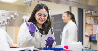 Woman with black hair and white lab coat, working with a syringe.