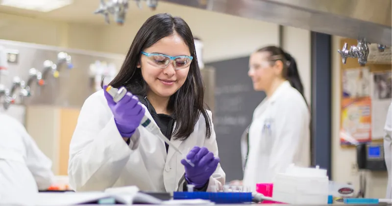 Woman with black hair and white lab coat, working with a syringe.