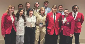 Group of students, wearing red blazers, black and brown pants, some with medals around their necks.