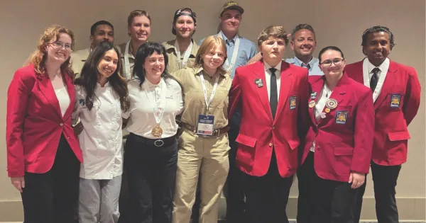 Group of students, wearing red blazers, black and brown pants, some with medals around their necks.
