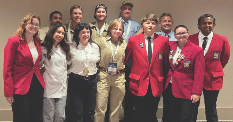 Group of students, wearing red blazers, black and brown pants, some with medals around their necks.