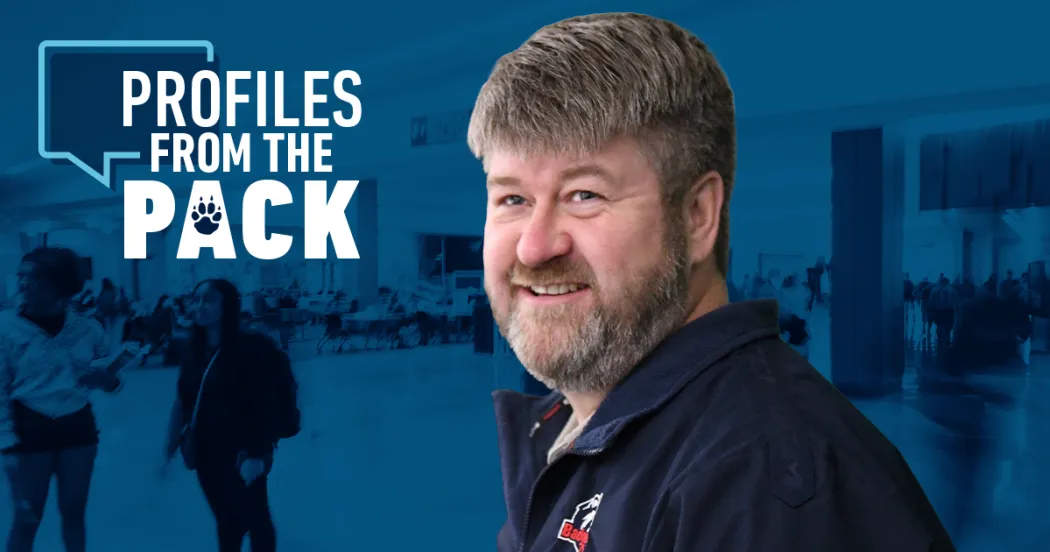 Photo of Miles Tokheim, wearing navy shirt, mustache and beard, smiling and looking at camera. 